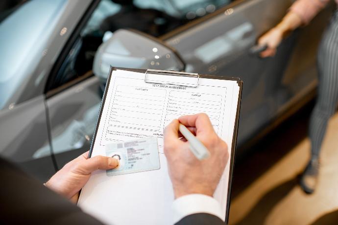 Duplicados Firma de documentos junto a un carné de conducir mientras de fondo un conductor se sube al coche de fondo