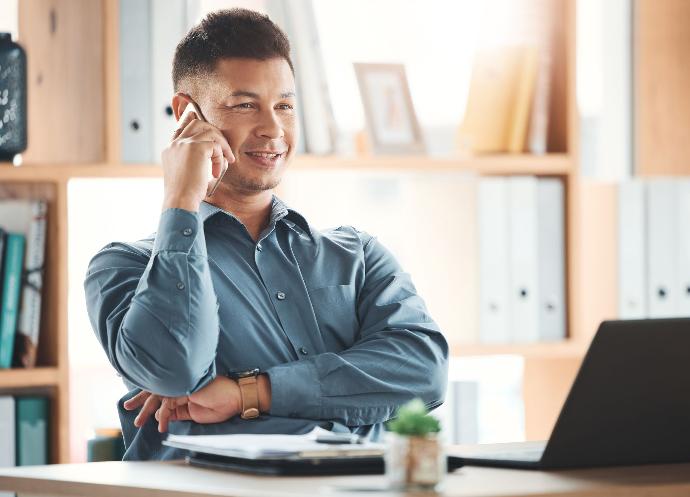 Subvenciones para la actividad empresarial Hombre teniendo una llamada telefónica en su despacho frente a su ordenador portátil y documentos en su mesa